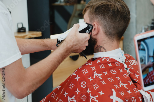 Handsome bearded man in barbershop. Barber cuts hair with  electric trimmer. photo