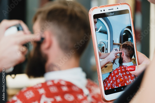 Handsome bearded man in barbershop. Barber cuts hair with  electric trimmer. photo