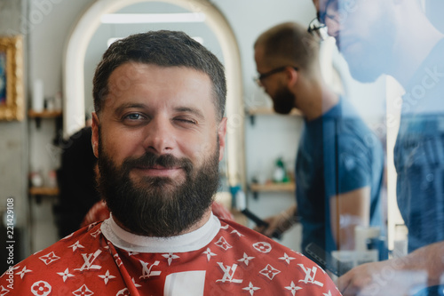 Mature handsome bearded smiling man in barbershop. Barber trimmes hair. photo