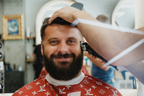 Mature handsome bearded smiling man in barbershop. Barber trimmes hair. photo