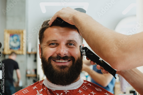 Mature handsome bearded smiling man in barbershop. Barber trimmes hair. photo