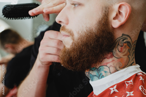 Skinhead bearded tattooed man in barbershop. Barber cuts hair with trimmer. photo