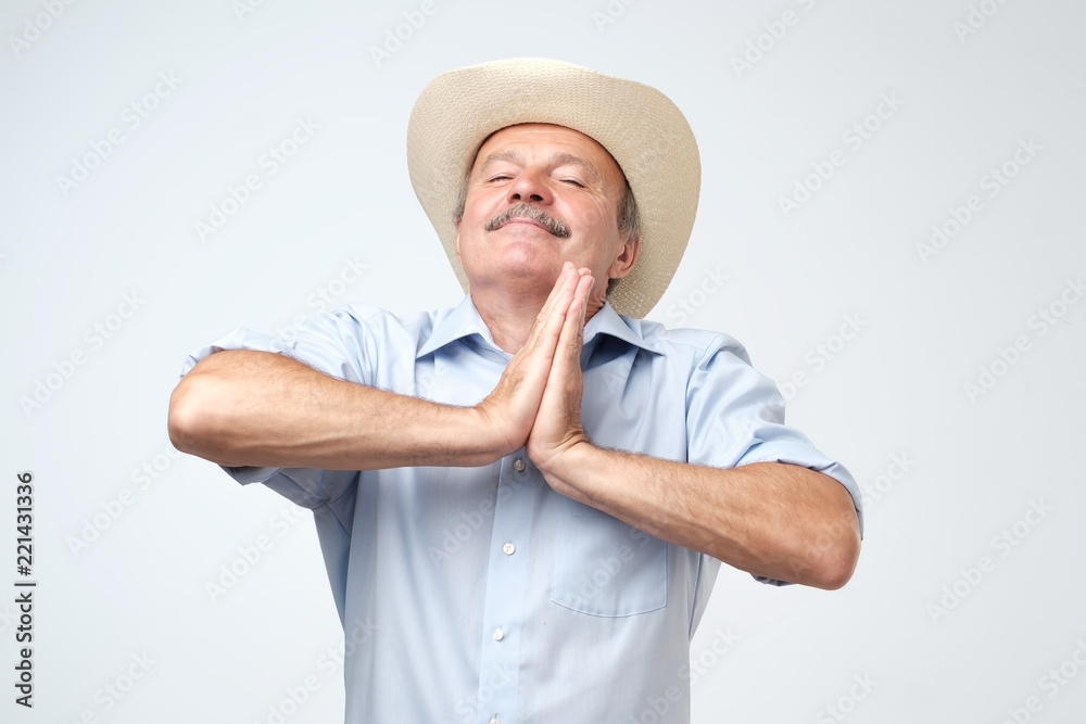 Pleased hopeful mature man closes eyes, keeps palms together, prays to have good luck, has dreamful look Pleased hopeful mature man closes eyes, keeps palms together, prays to have good luck, has dreamful look