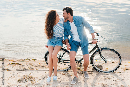 beautiful couple sitting together on bicycle on beach near sea