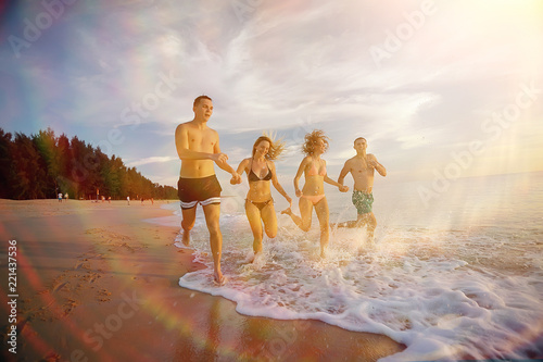 four friends are running on beach / summer vacation fun happiness, young men and women are running in the splashes of the sea along beach