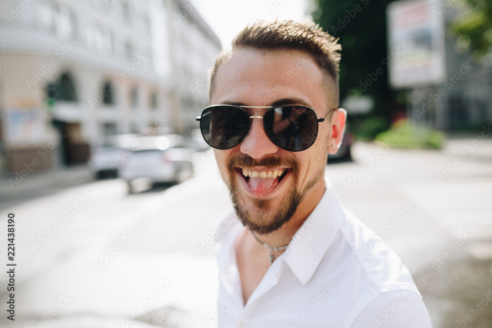 A young man in white shirt and sunglasses laughing happily outdoor. Street fashion.