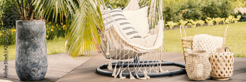 Hanging chair between lanterns and palm in stone vase on the terrace during spring. Real photo
