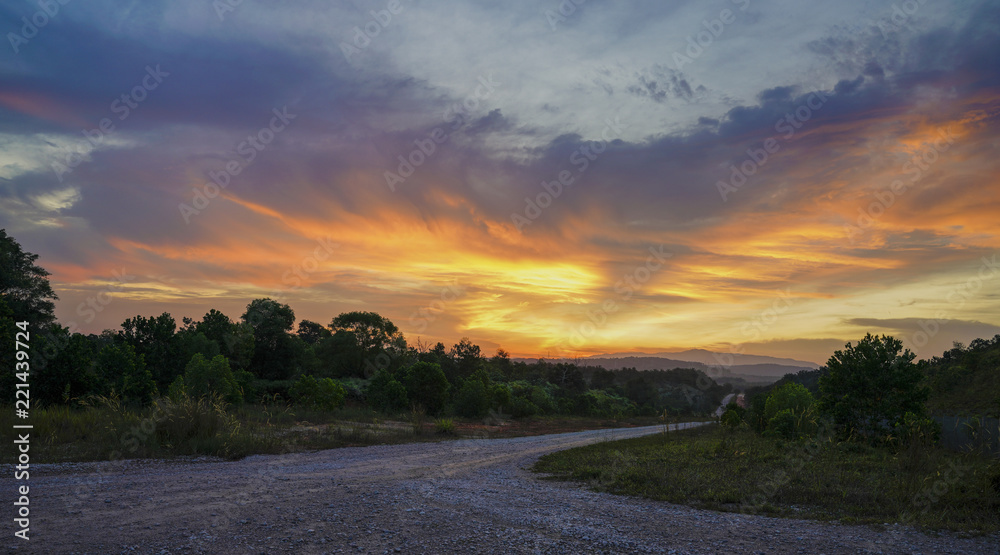 Empty gravel road against an orange sky at sunset