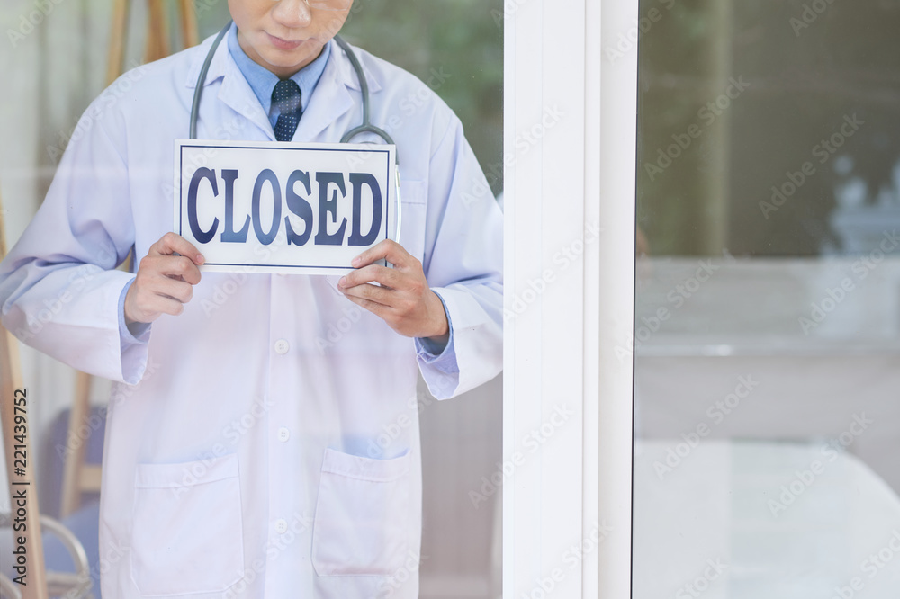 Anonymous guy in medical uniform holding sign with closed writing while standing behind glass in office - obrazy, fototapety, plakaty 
