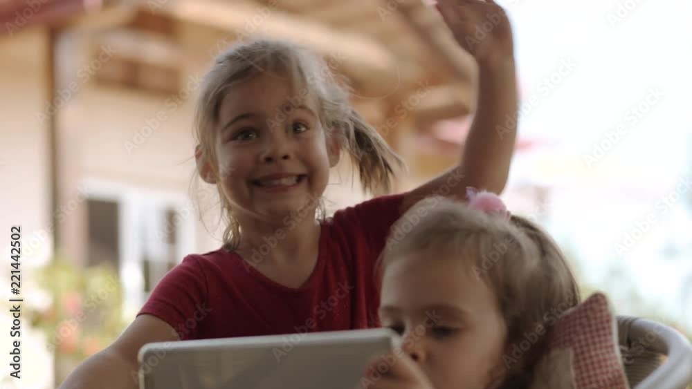 girl stands next to her sister and makes funny faces and waves her hand girl stands next to her sister and makes funny faces and waves her hand