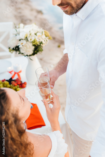 cropped view of couple clinking with champagne glasses during romantic date on seashore