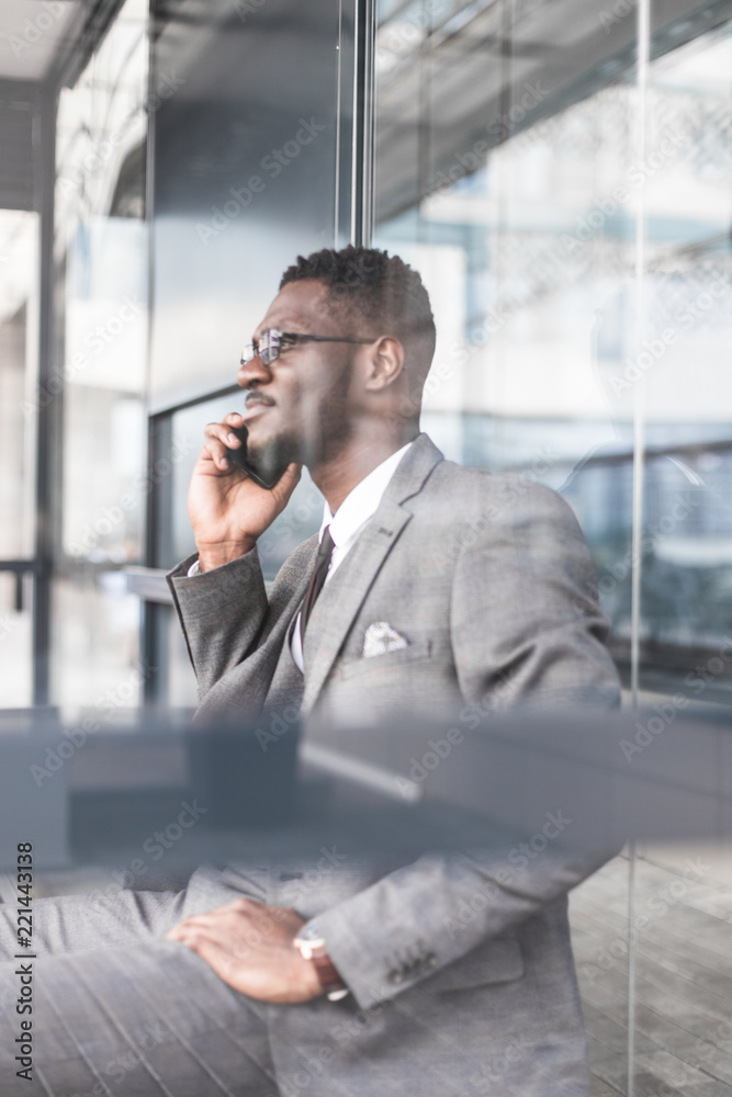 black man businessman in a business suit, expensive watch and glasses talking on the phone, decides business matters against the backdrop of a modern city to work black man businessman in a business suit, expensive watch and glasses talking on the phone, decides business matters against the backdrop of a modern city to work