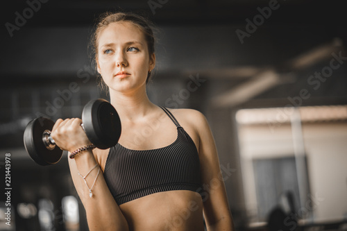 Fit beautiful young woman caucasian posing at the camera in sportswear. Young woman holding dumbbell during an exercise class in a gym. Healthy sports lifestyle, Fitness concept. With copy space.