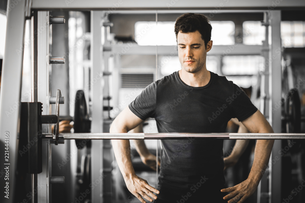 Fit caucasian handsome young man and big muscle in sportswear. Young man standing and looking machine weight lifting in a gym. Healthy sports lifestyle, Fitness concept. with copy space