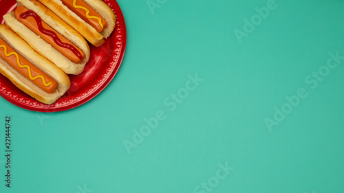 Three hot dogs on a red plate mustard ketchup background with copy space