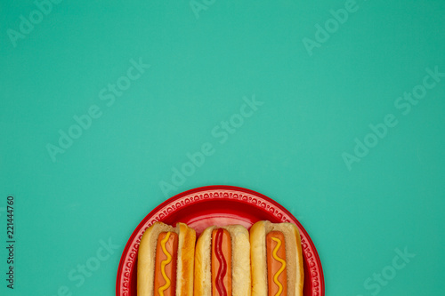 Three hot dogs on a red plate mustard ketchup background with copy space