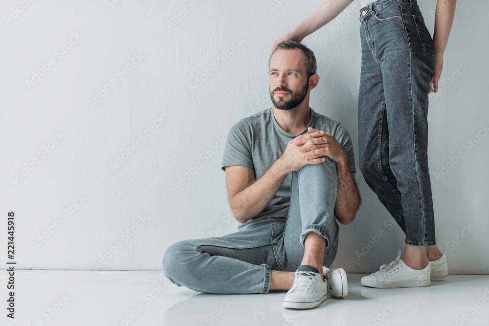 cropped shot of young woman touching frustrated bearded man sitting on floor and looking away