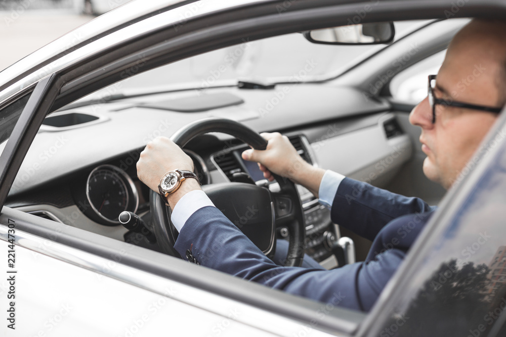 a businessman driving a prestigious car holds a mobile phone in his hand. Hasty life