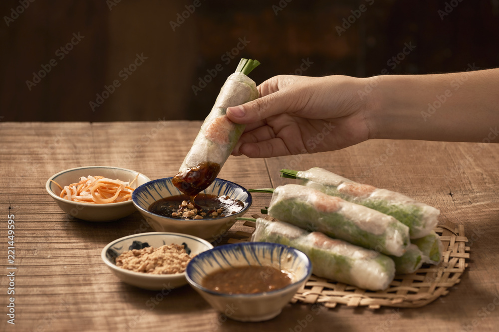 Hand holding Vietnamese spring roll above the bowl with dipping soy sauce