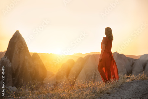 A girl in a red dress in the sunlight against the backdrop of pointed rocks. very light artistic photo. Cappadocia. Turkey. 