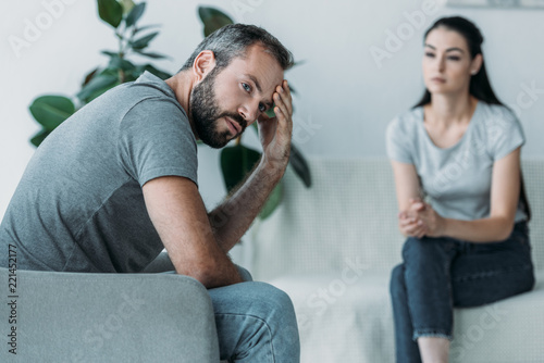 Φωτογραφία upset middle aged man sitting on couch and girlfriend sitting behind