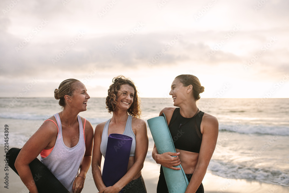 Three women carrying yoga mats standing at the beach Three women carrying yoga mats standing at the beach