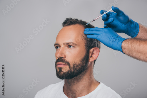 cropped shot of doctor with syringe giving injection to man with alopecia looking away isolated on grey photo