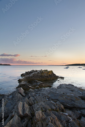 Boats sitting at anchor in Kettle Cove, Main during sunset with a rocky peninsula in the foreground. © Jason Yoder
