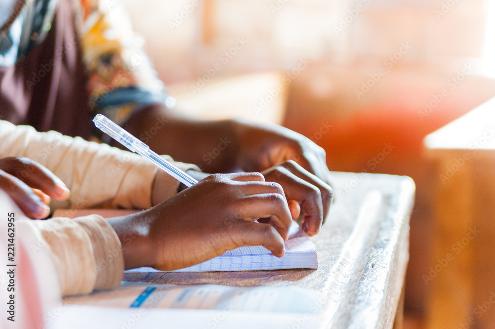 Obraz premium hands of young african school boys and girls during lesson in classroom with bright sun light holding pen and writing