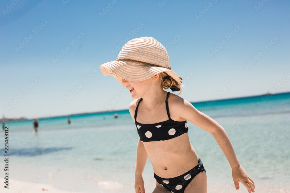little girl in big hat on summer tropical beach, wide panorama. little girl running barefoot on the white sand of the beach in a swimsuit and straw hat little girl in big hat on summer tropical beach, wide panorama. little girl running barefoot on the white sand of the beach in a swimsuit and straw hat