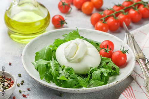 Delicious Italian fresh burrata cheese with arugula salad, cherry tomatoes and olive oil in a white plate. Gourmet snack