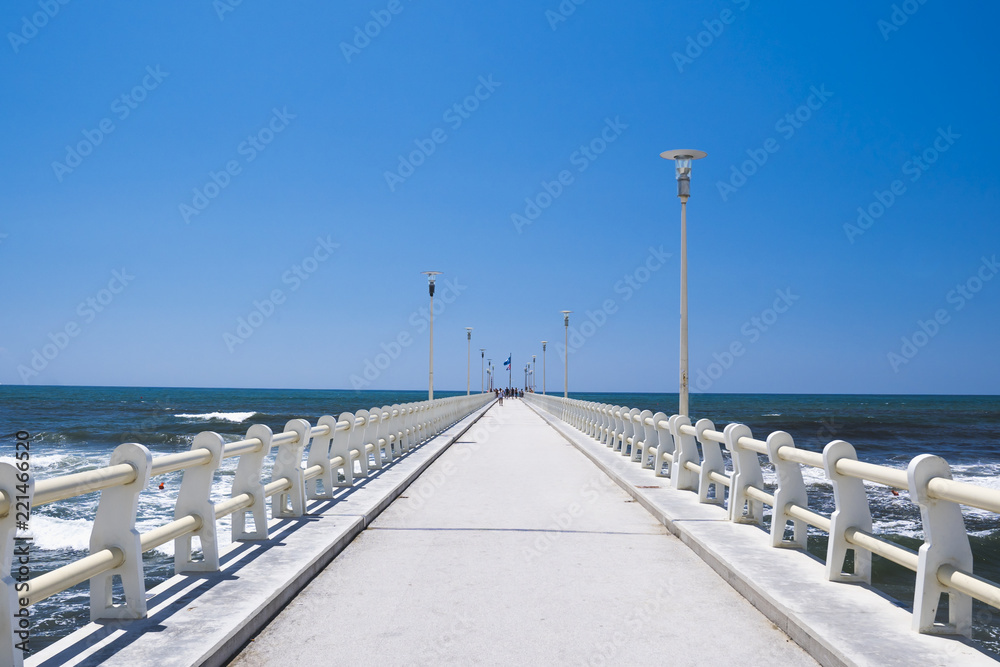 Long pier heading to the sea, in a sunny day with blue sky.