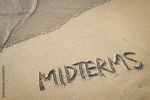 'MIDTERMS' written in the sand on the beach with the sea washing up the shore.  photo