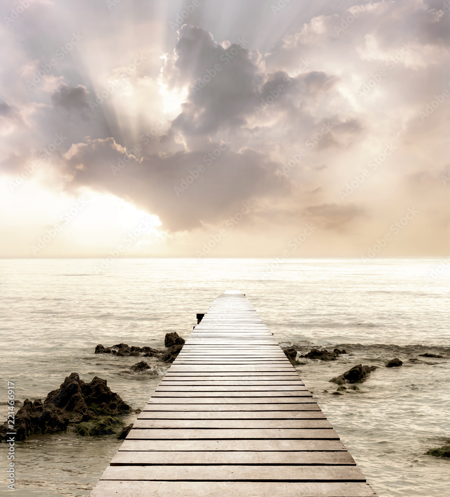Obraz premium Drewniany most na morzu, który ma drogę do podróży z pięknym niebem i słońcem w tle.