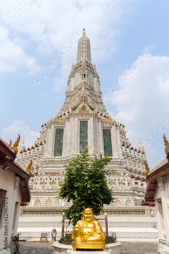 Golden statue of sitting Buddha and decorated Wat Arun temple viewed from the front in Bangkok, Thailand, on a sunny day.