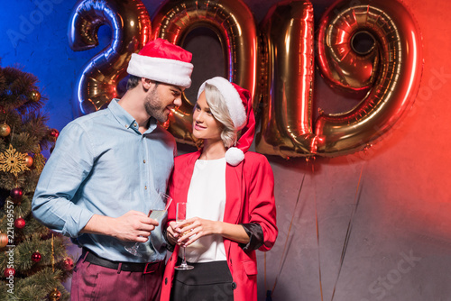 young businesspeople in santa hats looking at each other at new year corporate party