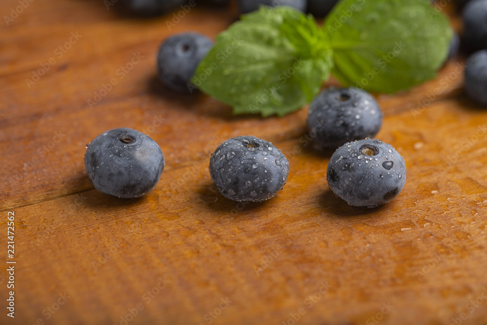 Juicy and fresh blueberries with green mint leaves on a wooden table. Blueberries on wooden background. Juicy and fresh blueberries with green mint leaves on a wooden table. Blueberries on wooden background.