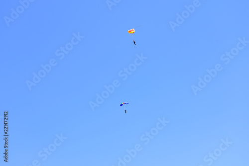 Two paratroopers descend against a blue sky