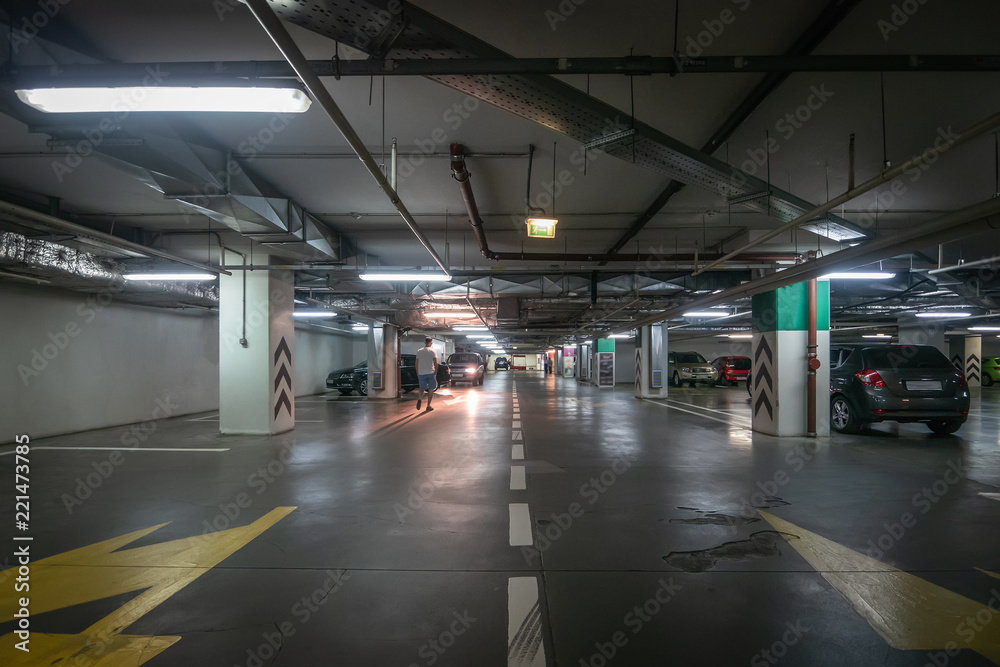 Large hall with columns of underground car parking garage with many automobiles in modern mall or shopping center