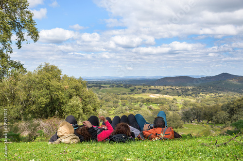 Group of people lying down looking towards the meadow in the shade of an oak tree on a beautiful spring day.