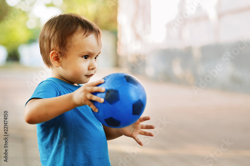 Fototapeta Naklejka Na Ścianę i Meble -  Portrait of a little boy playing with a ball outdoor. Child holding toy soccer ball and ready to throw it. Place for copy text