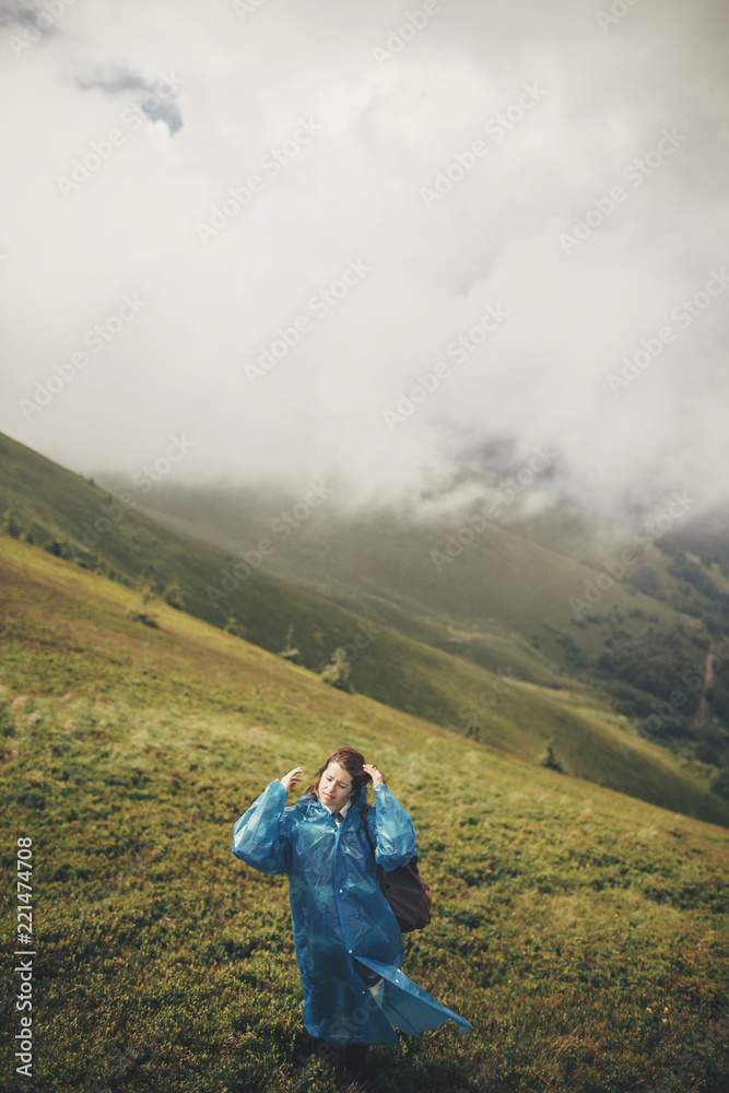 traveler hipster girl  in blue raincoat with backpack, exploring misty mountains. space for text. atmospheric moment. travel and wanderlust concept.  woman walking on hills