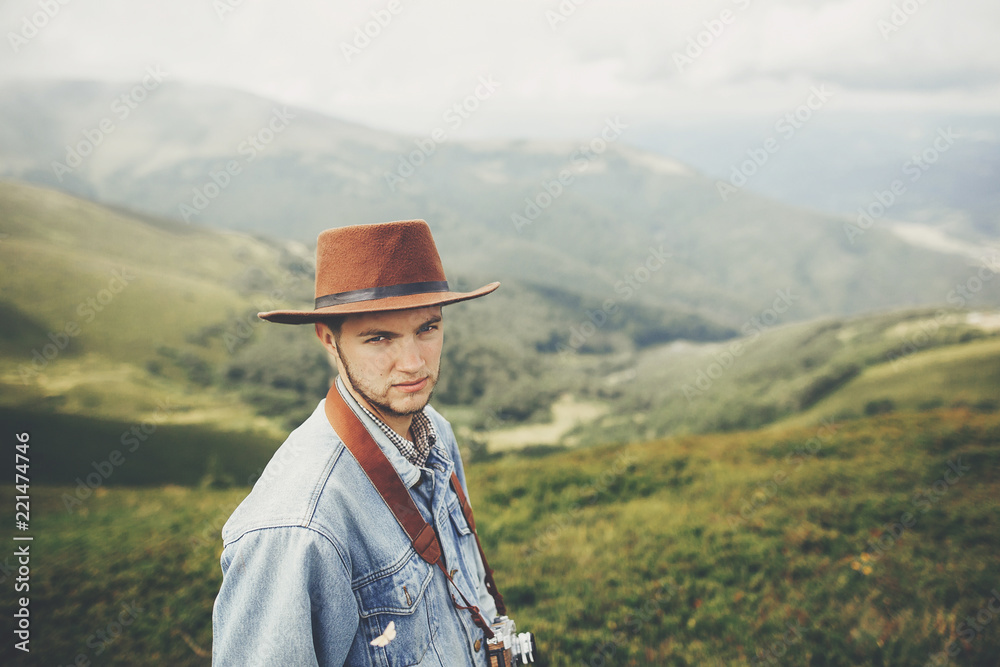stylish traveler man standing on top of mountains with photo camera in clouds. space for text. hipster guy traveling. amazing atmospheric moment. travel and wanderlust concept. stylish traveler man standing on top of mountains with photo camera in clouds. space for text. hipster guy traveling. amazing atmospheric moment. travel and wanderlust concept.