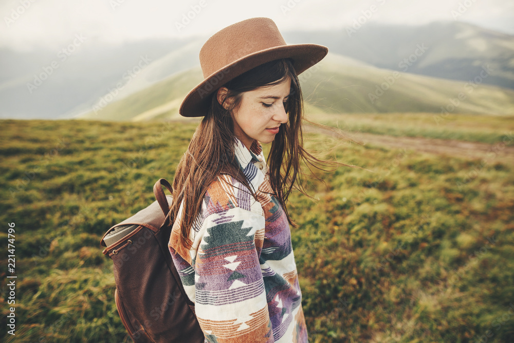 travel and wanderlust concept. traveler hipster girl in hat with backpack exploring misty sunny mountains in clouds. space for text. stylish woman traveling. amazing atmospheric moment.