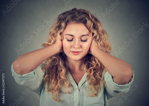Young woman covering ears avoiding noise on gray background