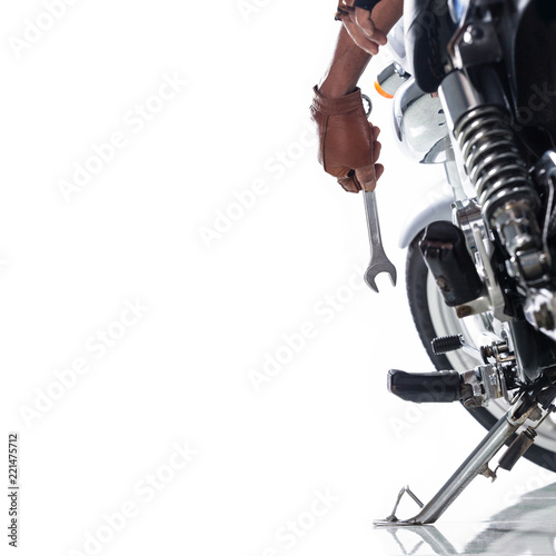 Cropped view of Mechanic using a wrench on a motorcycle on white background