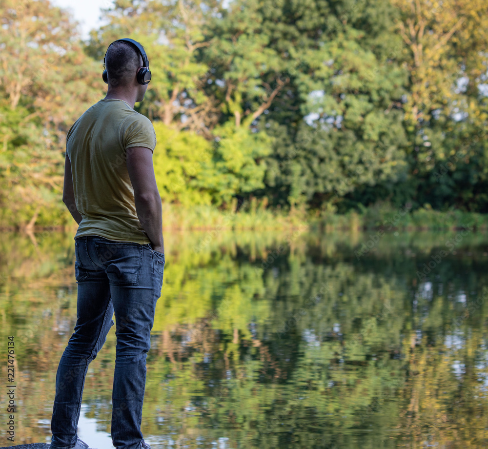 Mann mit Kopfhörern steht am Teich
