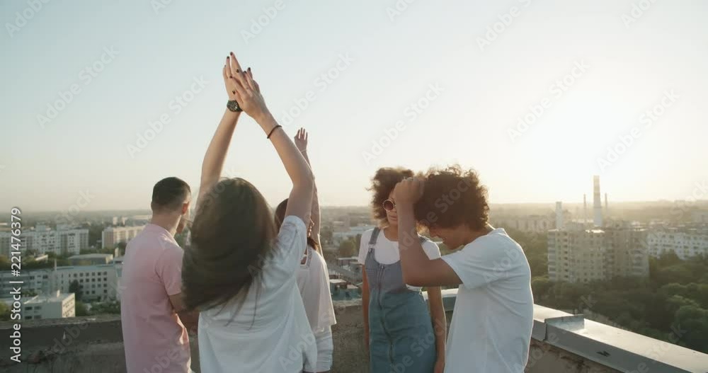 Five multiethnic friends enjoying their time, having summer roof party, talking, cheering, dancing to the music closeup 4k