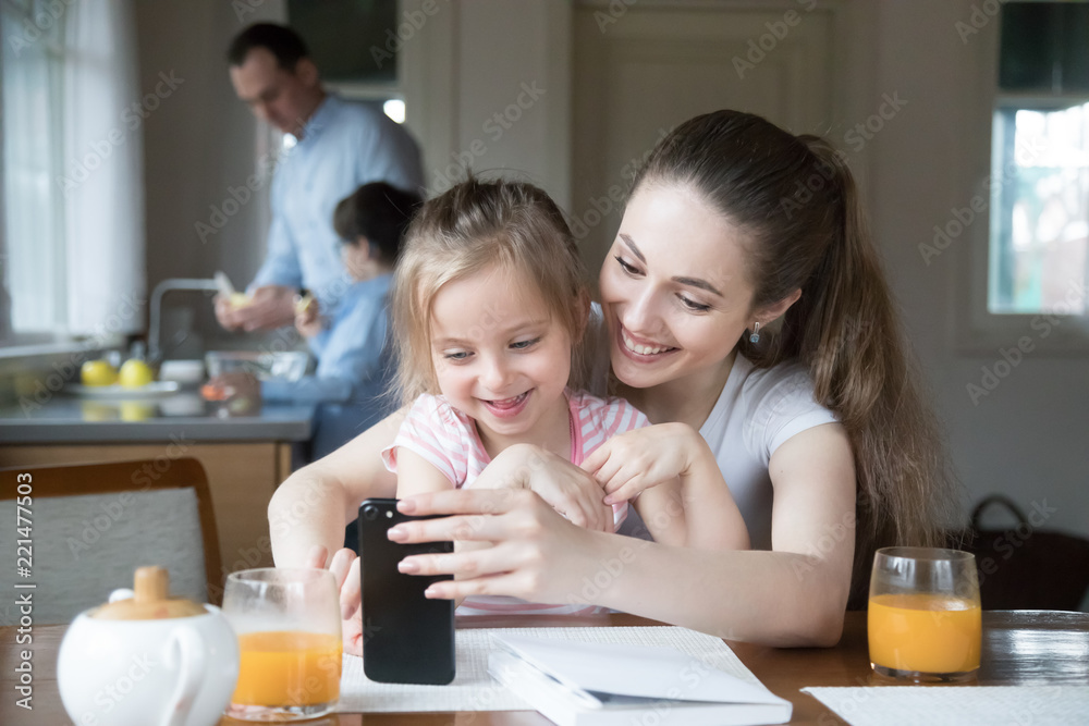 Happy mother and daughter having fun playing game on smartphone in kitchen, mom and girl spending time together watching cartoons or children video on phone, parent teach little kid using cell Happy mother and daughter having fun playing game on smartphone in kitchen, mom and girl spending time together watching cartoons or children video on phone, parent teach little kid using cell