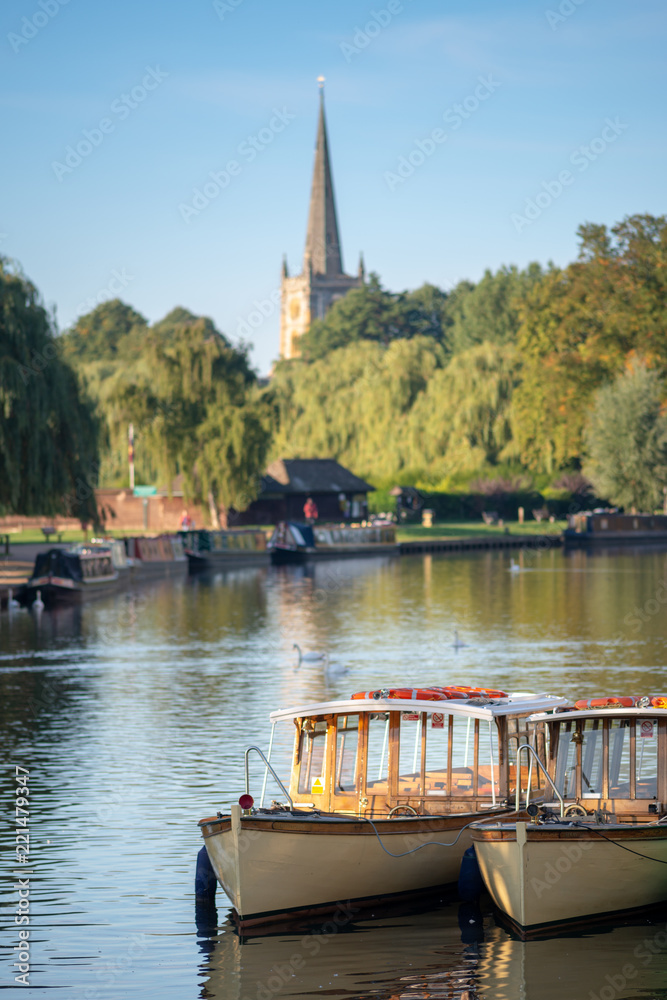 wooden edwardian boats moored up together in a typical English river scene in early autumn or fall with church in background